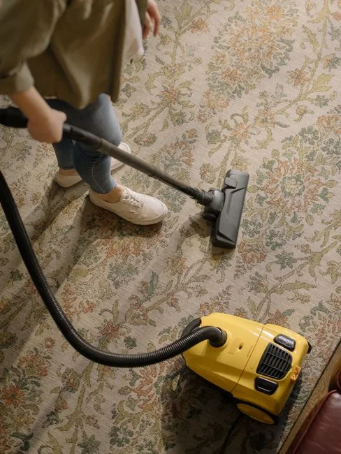 A professional cleaner in a red uniform holding a vacuum near a van, ready for service.